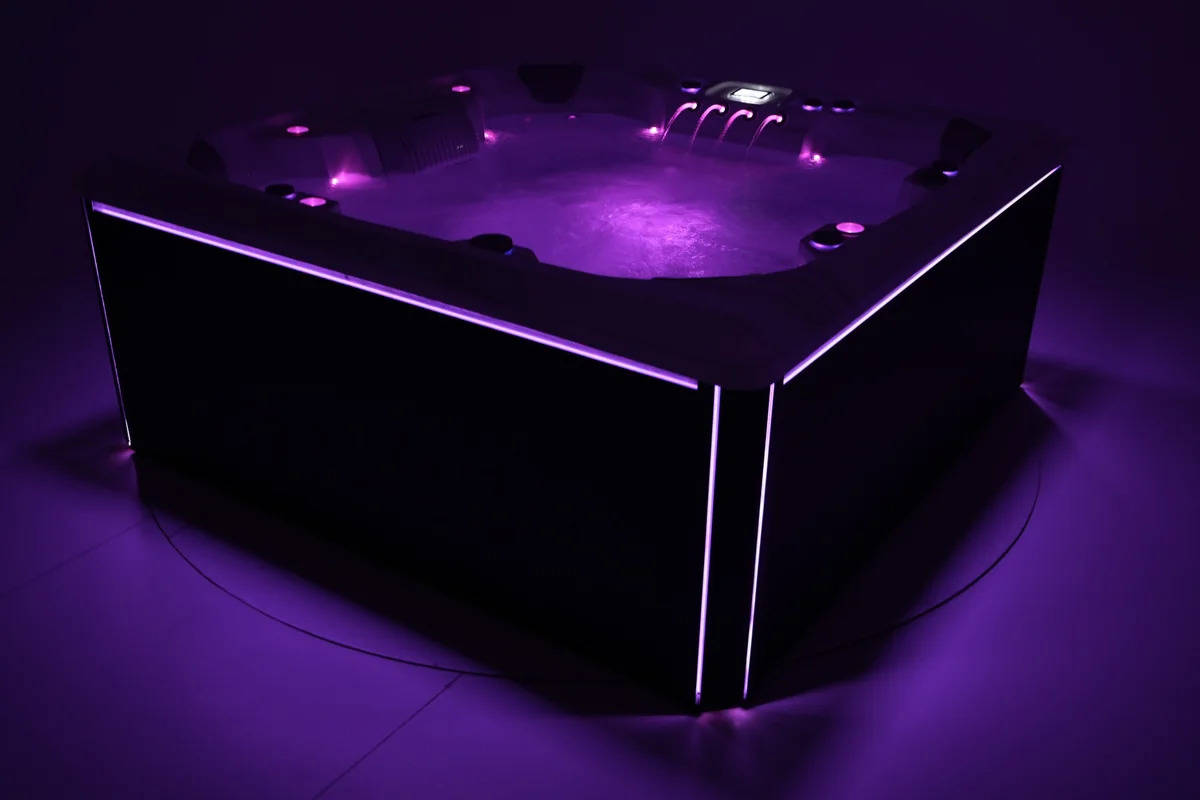 Backyard hot tub at night with path lighting, privacy landscaping, and clear walking space
