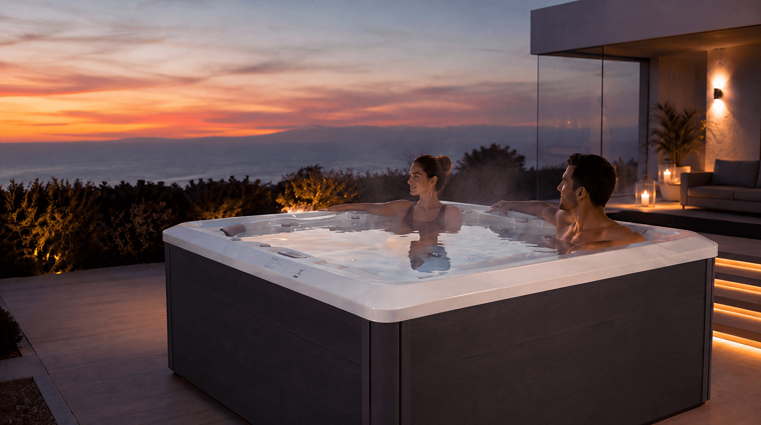 Two adults relaxing in a hot tub on a terrace at sunset